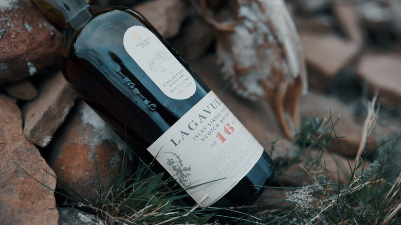 An outdoor shot of a bottle of Lagavulin 16-year placed against a pile of rocks