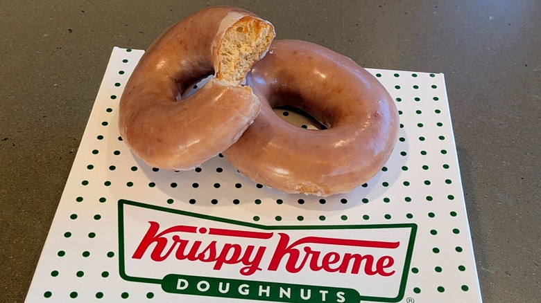 Two Apple Cider Original Glazed donuts, one with a bite taken out, on a Krispy Kreme box