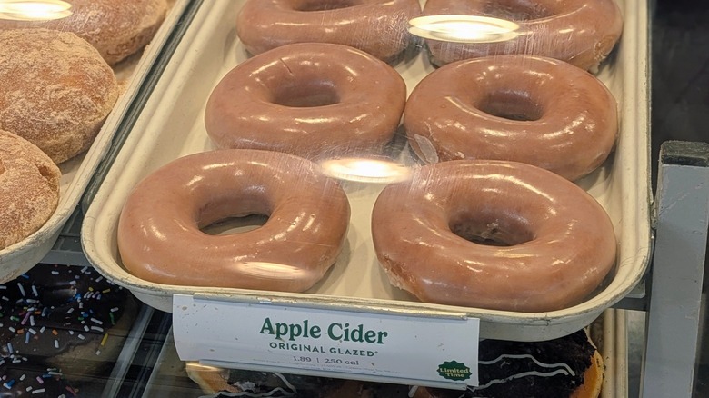A tray of shiny Apple Cider Original Glazed donuts inside the pastry case at Krispy Kreme