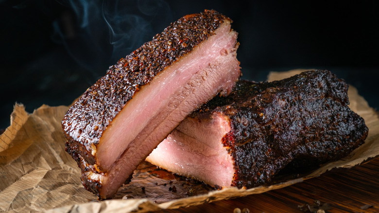 Two halves of whole cooked brisket with dark bard on the outside sitting on top of brown butcher paper