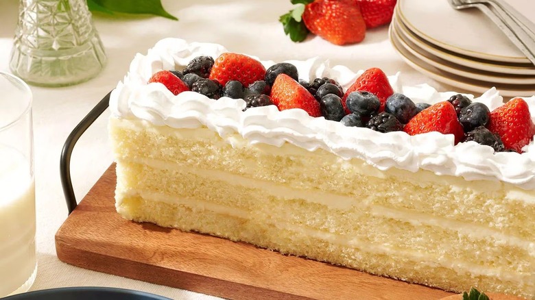 Member's Mark Fruit Topped Chantilly Cream Bar Cake from Sam's Club sitting on wooden board with plates, forks, and strawberries in the background