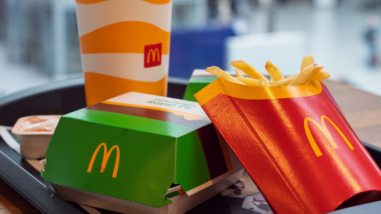 A meal from McDonald's featuring a sealed burger box next to some fries and a drink on a tray