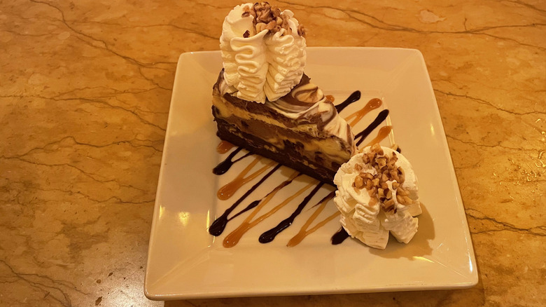 A decadent slice of chocolate cheesecake sits on a plate on a marble table.