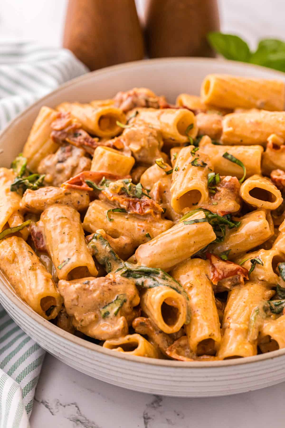 Close-up of creamy Tuscan chicken pasta in a bowl, showing rigatoni, spinach, and sun-dried tomatoes coated in Parmesan cream sauce.
