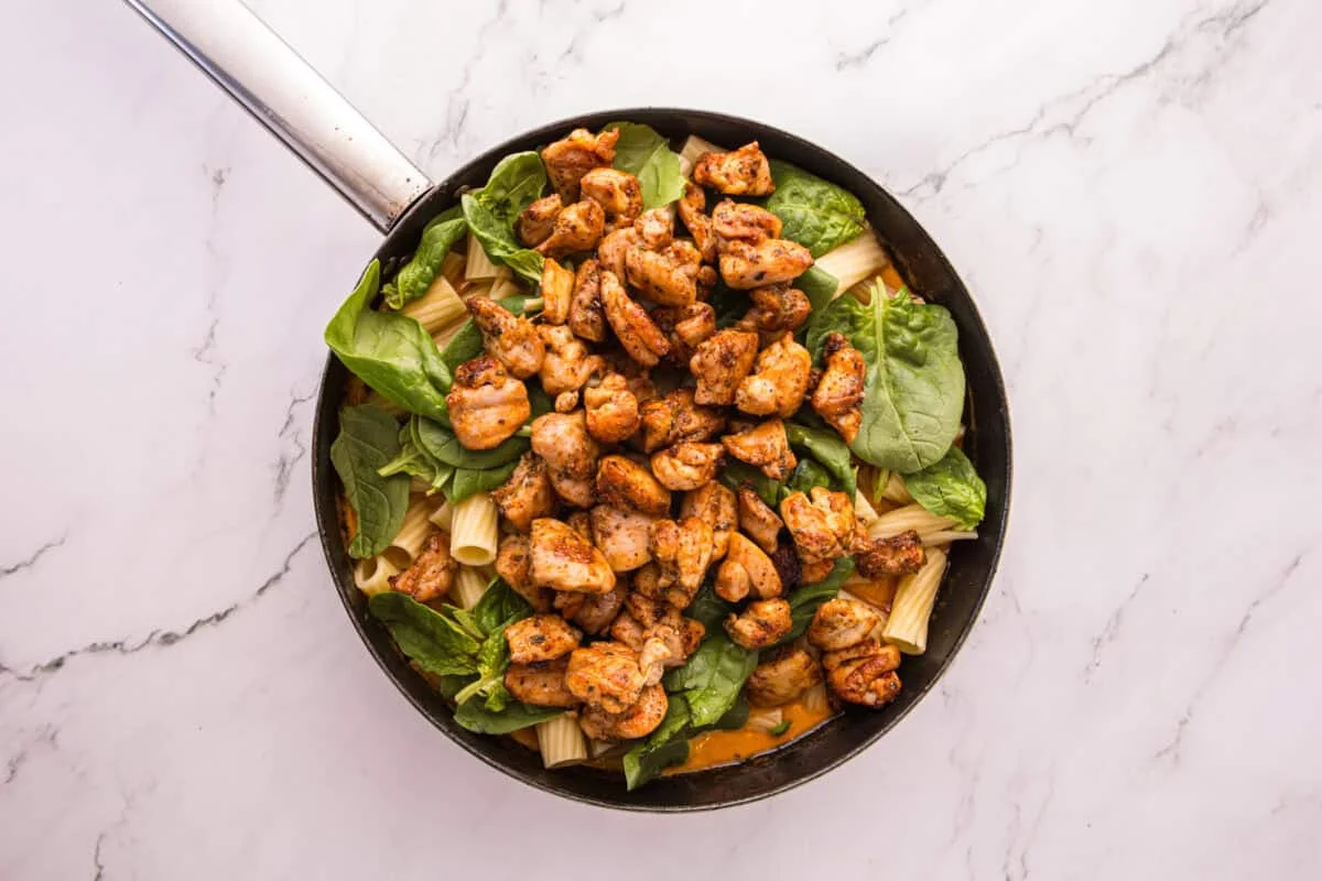 Cooked rigatoni, baby spinach, and seared chicken piled into the skillet before tossing with the sauce.