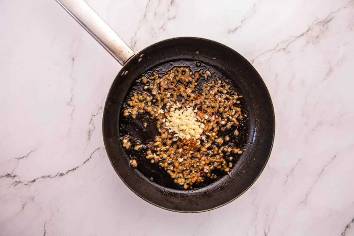 Chopped shallot, minced garlic, and red pepper flakes sautéing in a skillet.