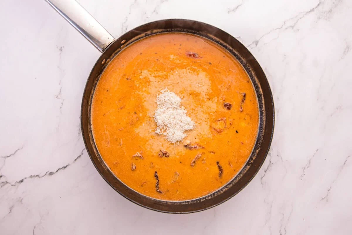 Freshly grated Parmesan added to the creamy Tuscan sauce in a skillet.