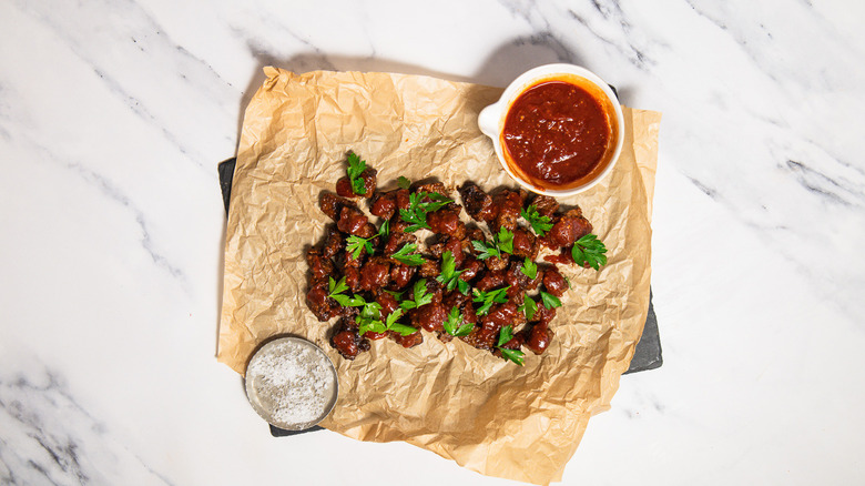 Steak bites on tray with parchment paper next to sauce and salt