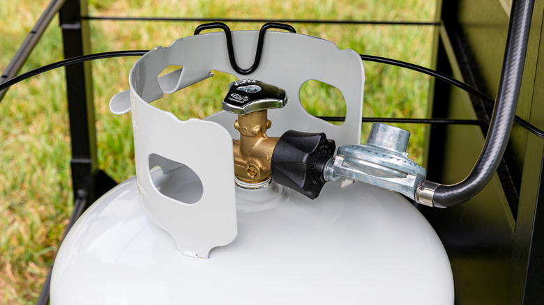 A white propane tank with regulator and hose assembly
