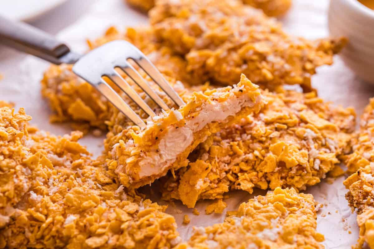 A fork cutting into a crispy cornflake chicken tender, revealing the juicy interior