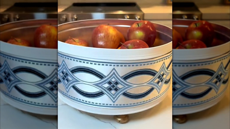 Repurposed cookie tin with legs storing apples