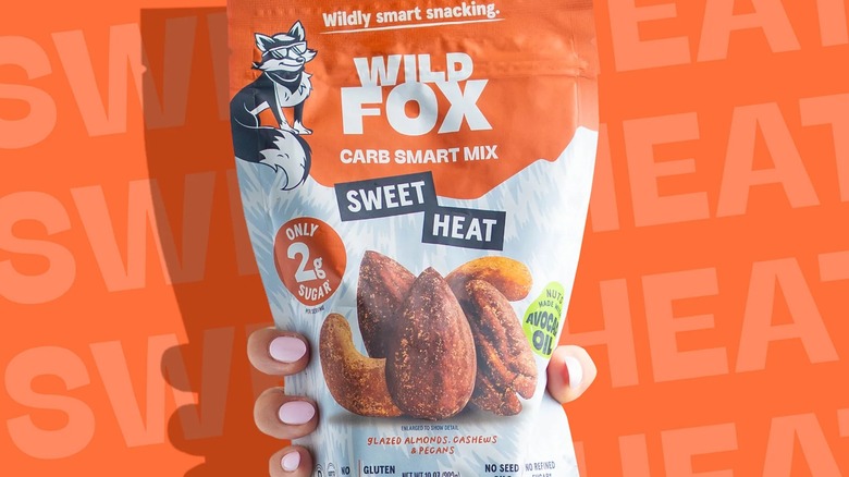Hand holding bag of Wild Fox Sweet Heat Carb Smart Mix with images of seasoned nuts on front