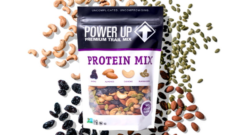 Bag of Power Up Protein Mix surrounded by cashews, raisins, pumpkin seeds, and almonds