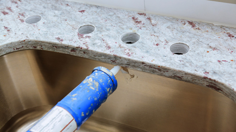 Sealant being applied around a sink installed beneath a stone countertop