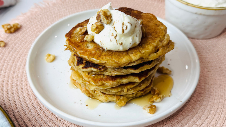 Carrot cake pancake stack on plate topped with cream cheese, syrup, and walnuts