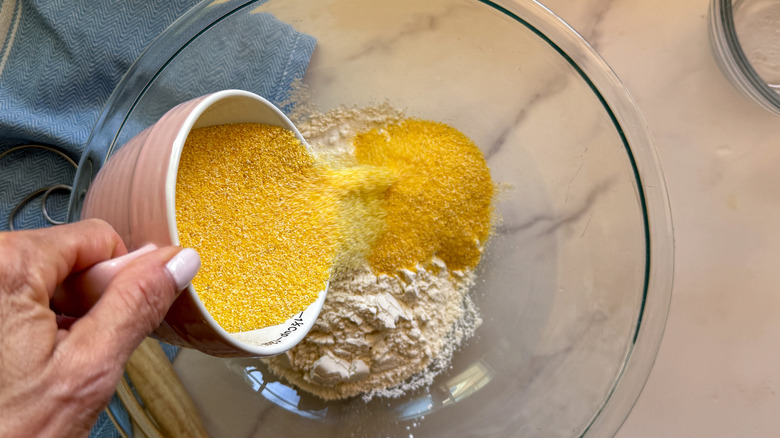 hand adding cornmeal to bowl
