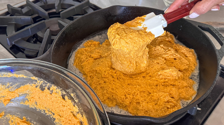 hand adding pumpkin cornbread batter to skillet
