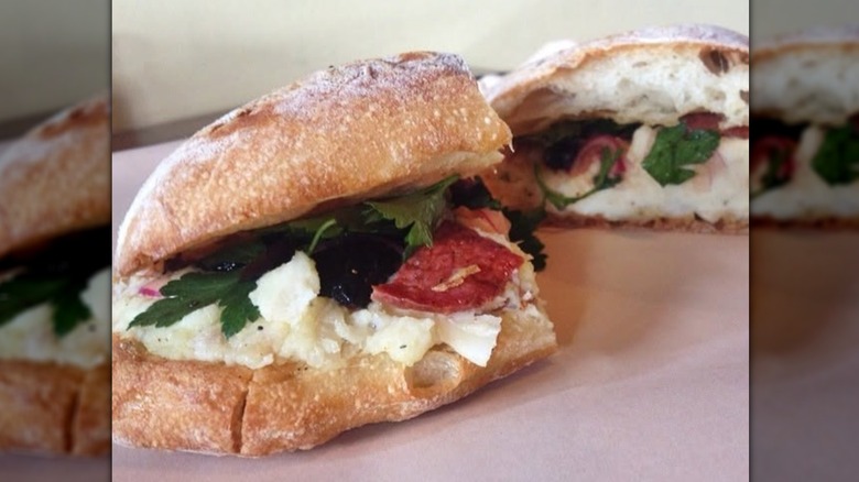 Halved salt cod sandwich, layered with chunky cod, chorizo, olives, and herbs