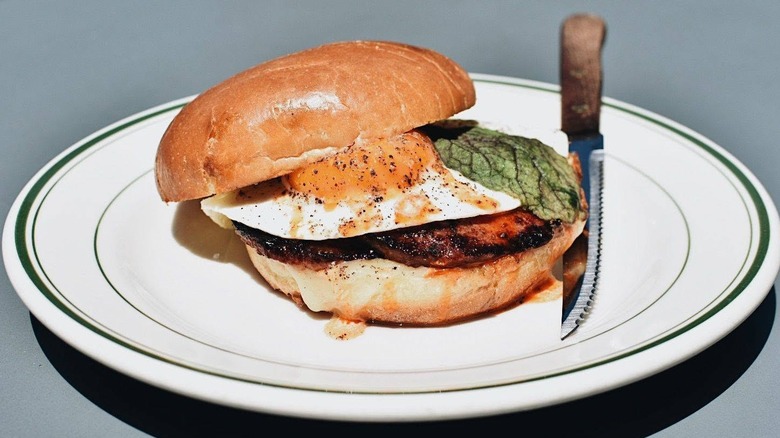 Fried bologna sandwich with a fried egg on a bun sitting on a white plate with a steak knife