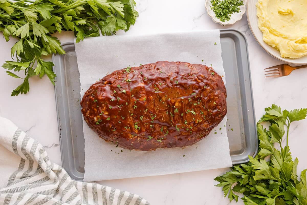 Baked stovetop stuffing meatloaf topped with a caramelized glaze and fresh parsley, served with mashed potatoes