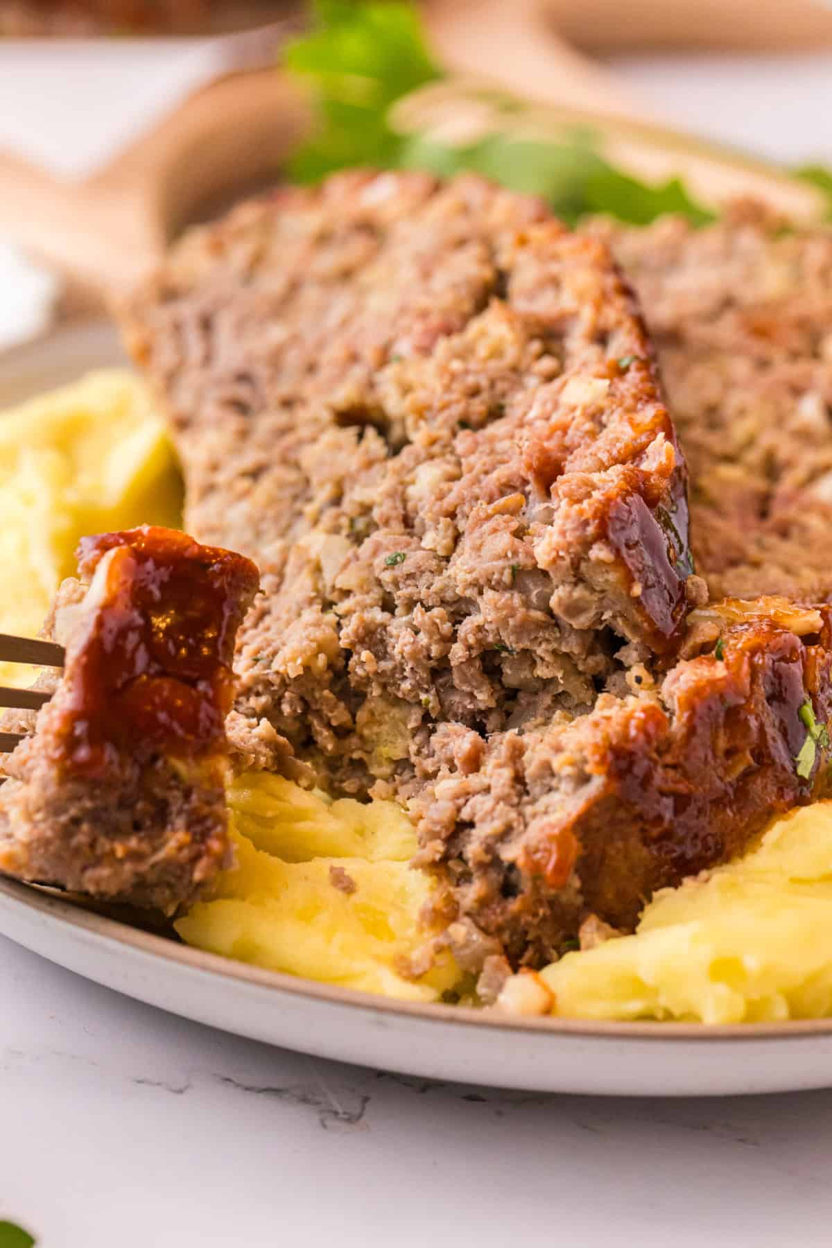 Close-up of a forkful of stovetop stuffing meatloaf with mashed potatoes on a plate