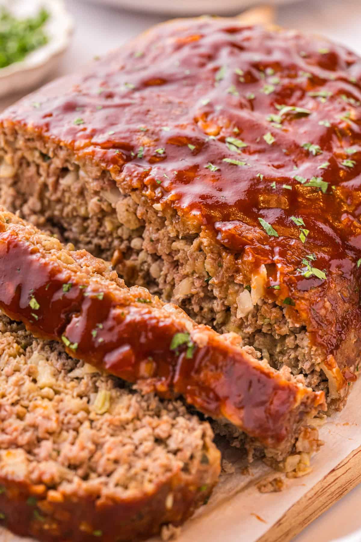Sliced stovetop stuffing meatloaf with a glossy ketchup glaze and parsley on a cutting board
