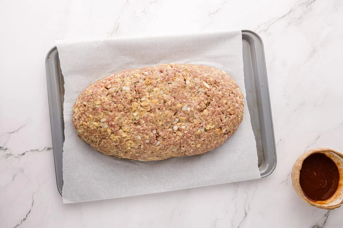 Raw stovetop stuffing meatloaf shaped into a loaf on a parchment-lined baking sheet