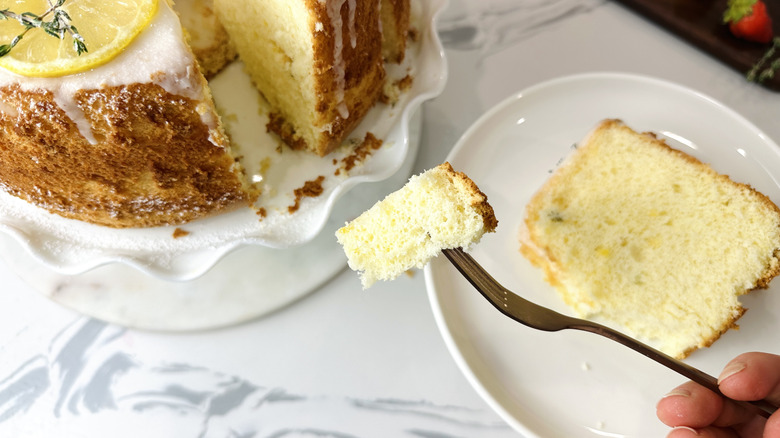 Fork holding bite of cake with whole cake and slice on plate in background