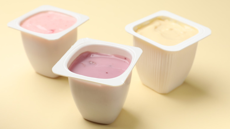 Three cups of flavored yogurt pictured on a pastel yellow background.