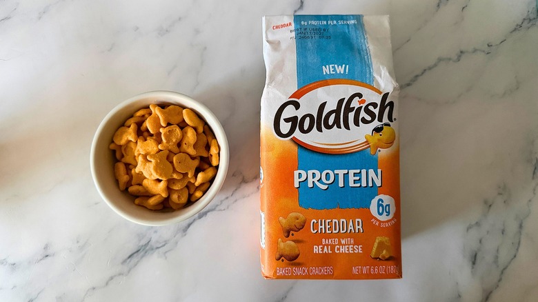 Bag of Cheddar Protein Goldfish next to small bowl of Goldfish on marble surface