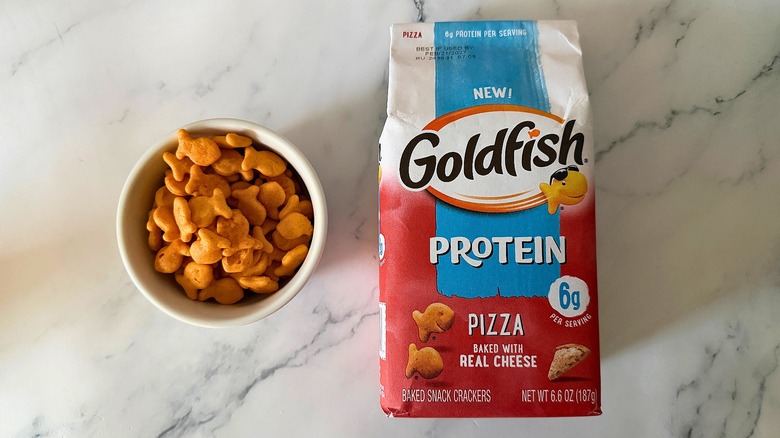Bag of Pizza Protein Goldfish next to small bowl of Goldfish on marble surface