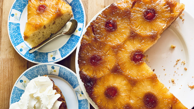 Pineapple upside down cake with candied cherries cut into two slices, one slice topped with whipped cream