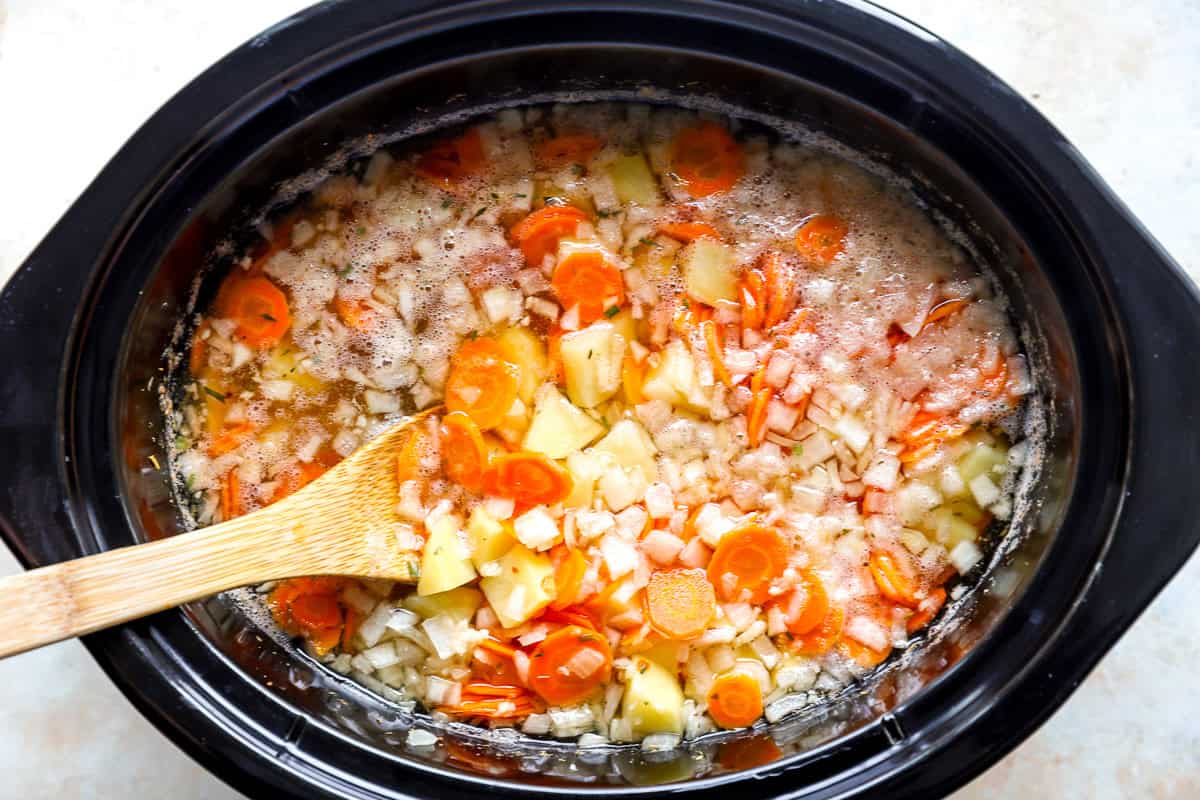 Potatoes, carrots, diced onion, and broth stirred together in a slow cooker before cooking.