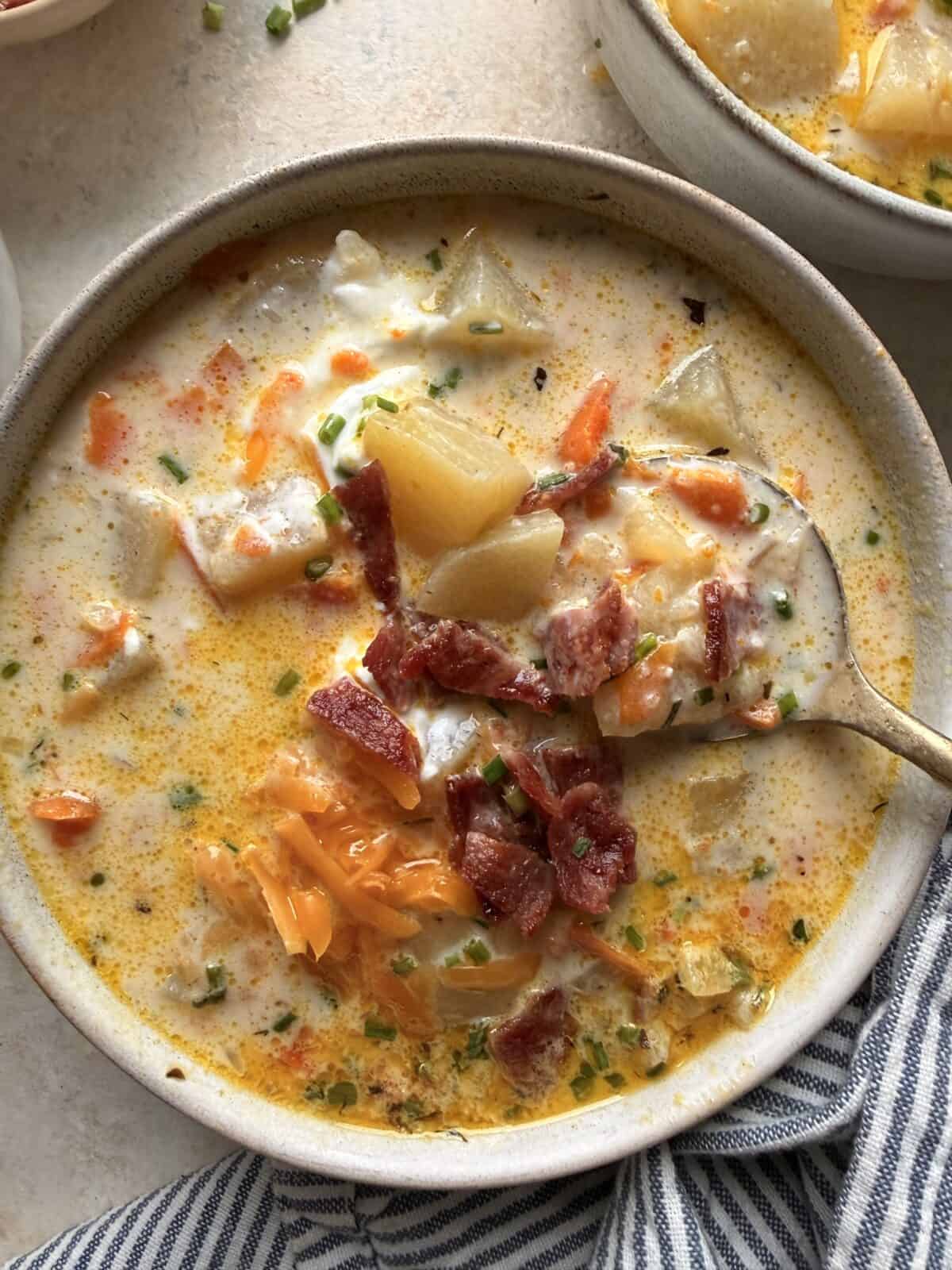 Close-up of a bowl of creamy potato soup with potato and carrot chunks, topped with turkey bacon, cheddar, sour cream, and chives.