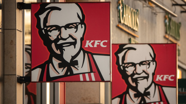 Two signs with the KFC mascot, hung on a building.