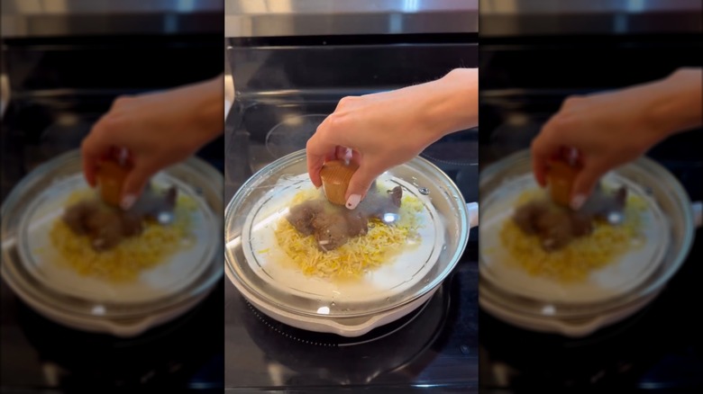 Hand holding lid over pan of food on stove