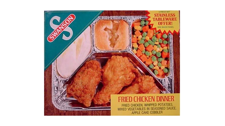 A Swanson TV dinner box featuring a fried chicken dinner with mashed potatoes, mixed veggies, and an apple cake cobbler in an aluminum tray on a white background