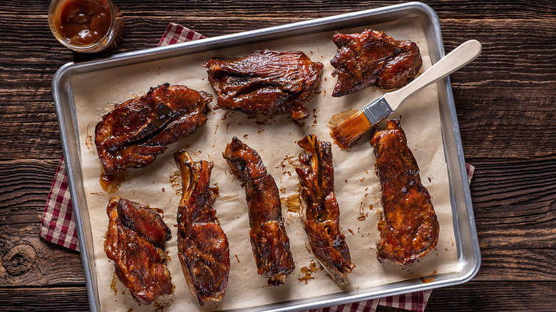 A brush with sauce lying next to a tray of country-style pork ribs