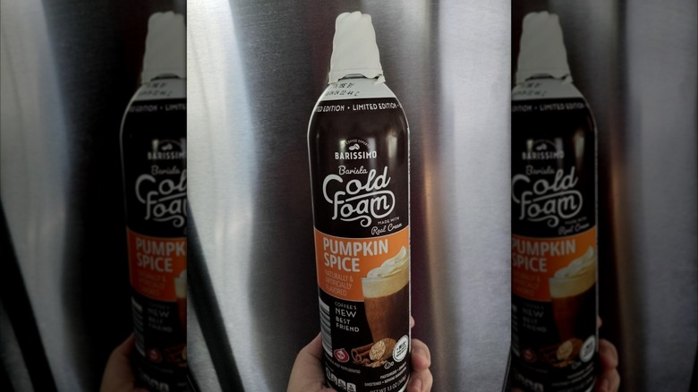 A person holding up a spray can of Aldi Barissimo Barista Pumpkin Spice Cold Foam