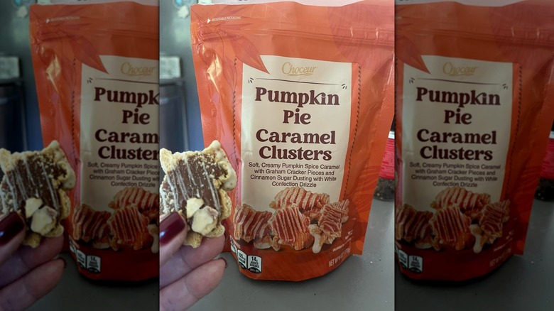 A person holding up a Choceur Pumpkin Pie Caramel Cluster next to an orange bag of the product