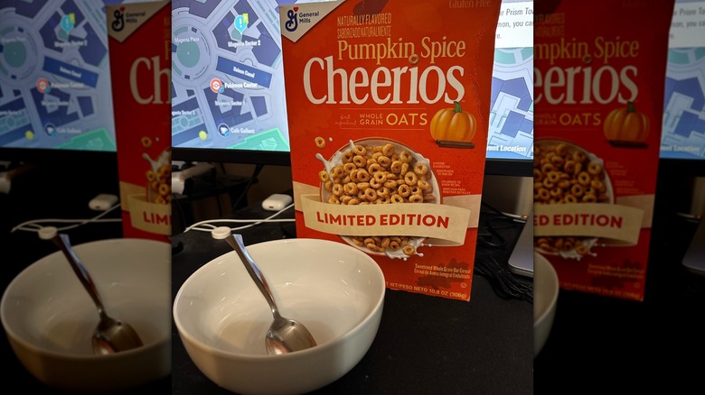 A box of General Mills Pumpkin Spice Cheerios on a computer desk next to a white bowl and spoon