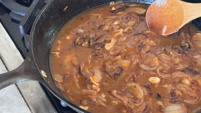 Wooden spoon stirring brothy onion mixture in skillet