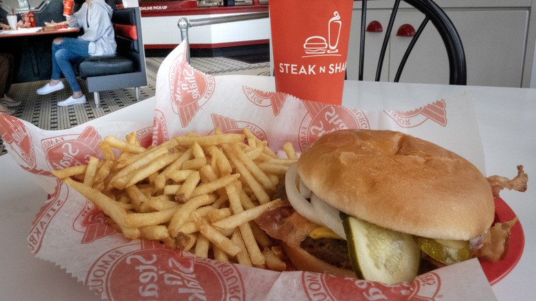 A Steak 'n Shake bacon cheese burger with fries and a soda sit on a table in the restauraunt's dining room