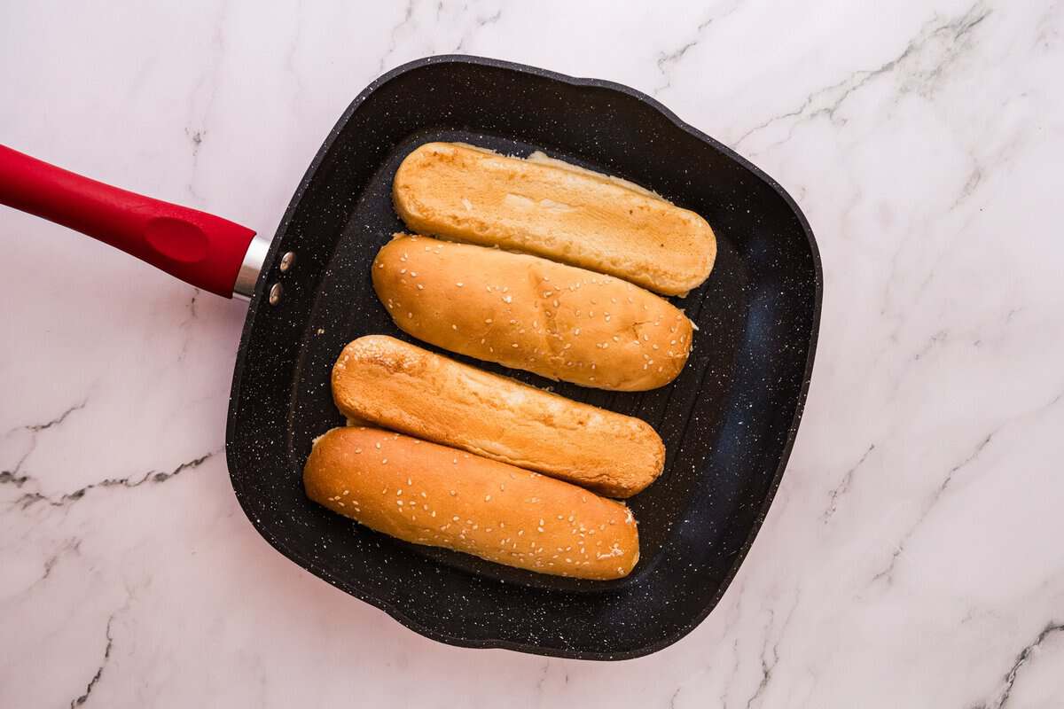 Sesamhoagie-ruller ristes skald-side ned i en sort grillpande med en rød håndtag.