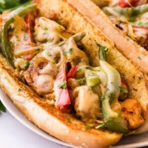 Close-up of a chicken cheesesteak on a garlic butter toasted hoagie roll, loaded with seared chicken, red and green bell peppers, caramelized onions, and melted provolone, garnished with chopped parsley.
