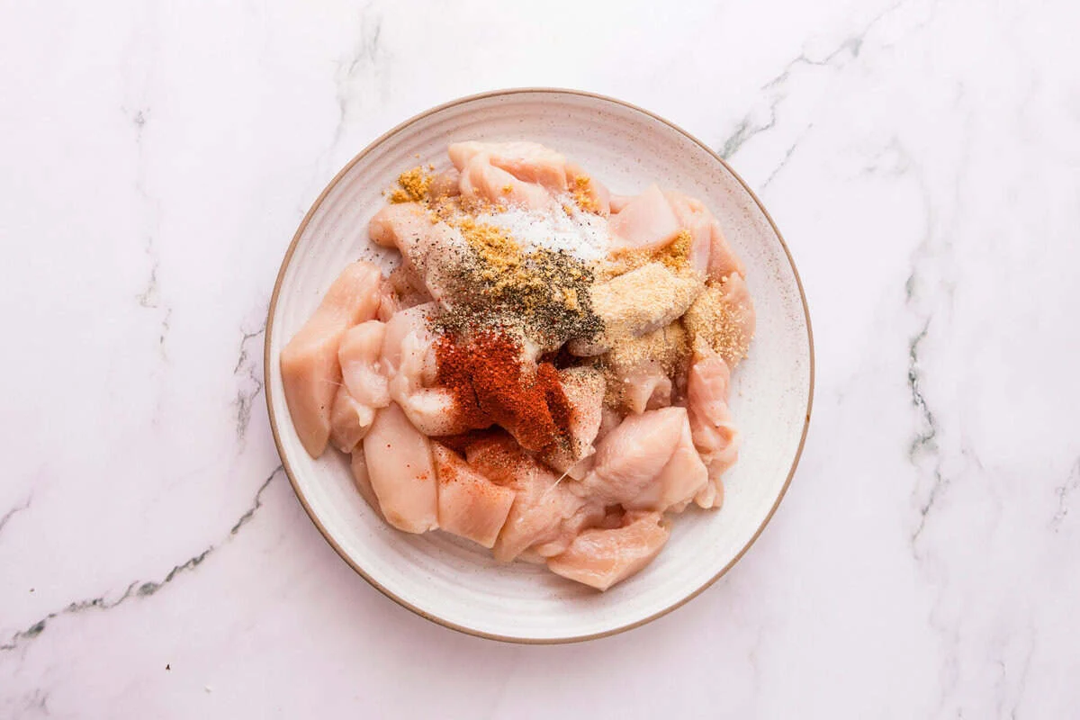 Rå skivede kylling Tenderloins på en tallerken toppet med salt, sort peber, hvidløgspulver, løgpulver og røget paprika.