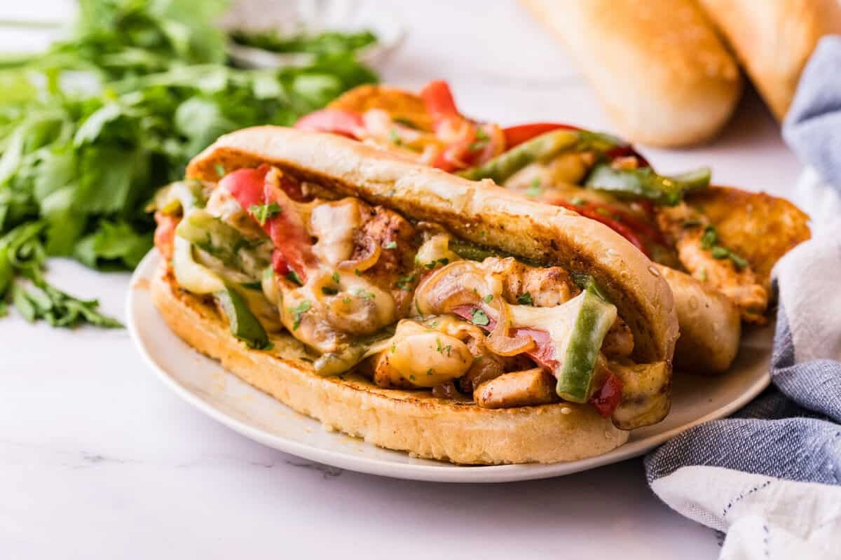 Sideprofil af en kylling-cheesesteak med provolone, der trækker sig ud over kylling og peberfrugter i en ristede hoagie-rulle.