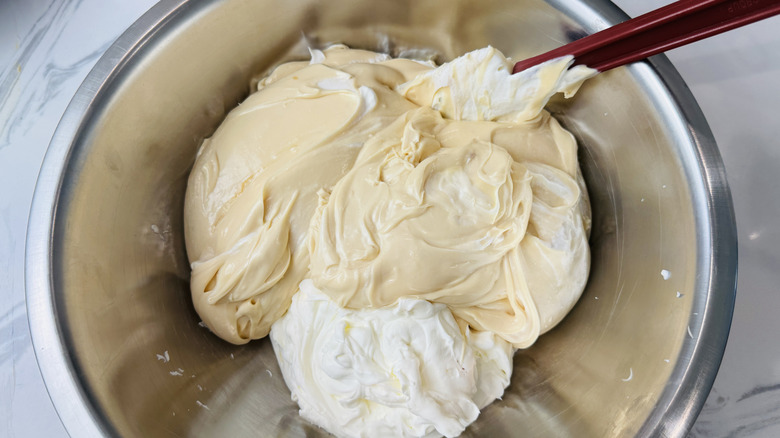 Caramel cream cheese mixture and whipped cream being mixed in bowl