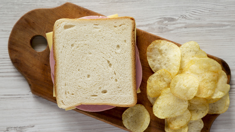 Bologna and cheese sandwich on a wooden board with potato chips