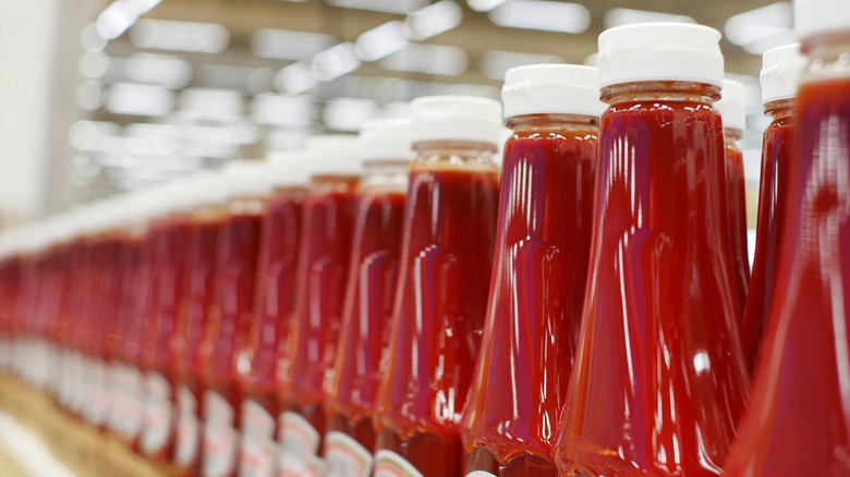 Many bottles of ketchup standing in a row in a factory